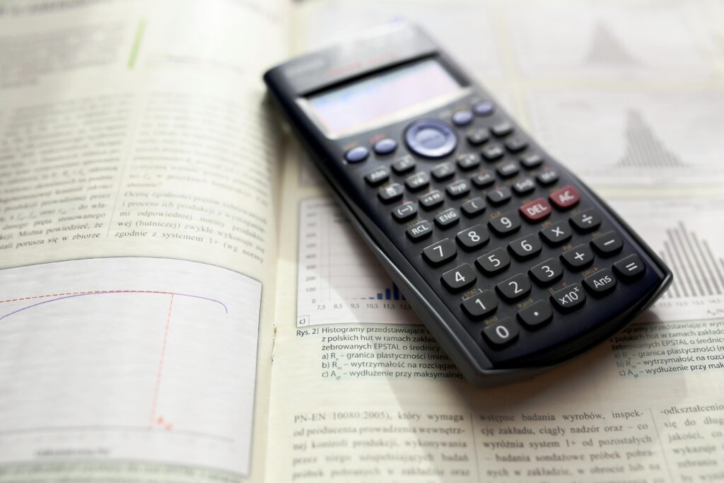 A graphing calculator rests on an open mathematics book with graphs and equations from LHtutoring