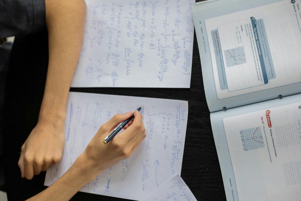 Top view of anonymous person with pen taking notes on piece of paper while solving equations in classroom during lesson with LHtutoring.